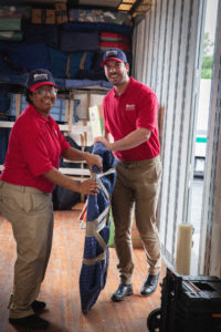 Wheaton movers carefully moving a wrapped-up piece of furniture.