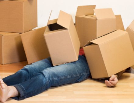 Sick or tired man laying face-up under a pile of cardboard moving boxes in an unfurnished room