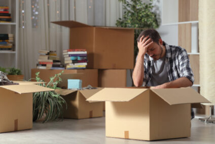 A man looks down at a moving box with his head in his hands.