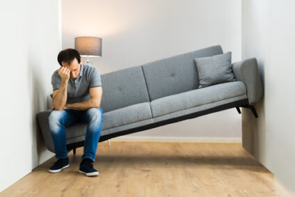 A man sits on a sofa that's stuck in a space that's too small.