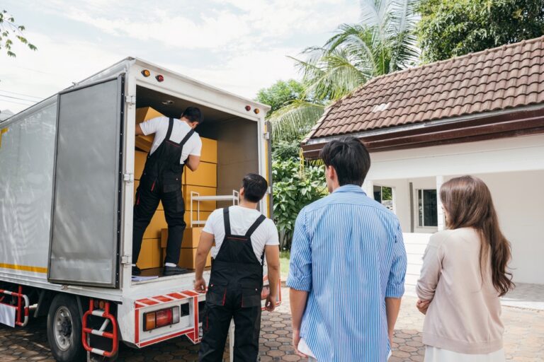 A young couple watches movers load a moving truck with boxes.
