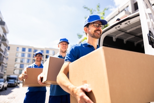 Three movers wearing blue polos and hats carry boxes into a moving truck.