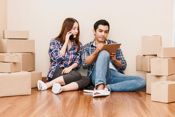 Couple sitting in a room full of boxes doing their moving prep: making a checklist and calling their moving company