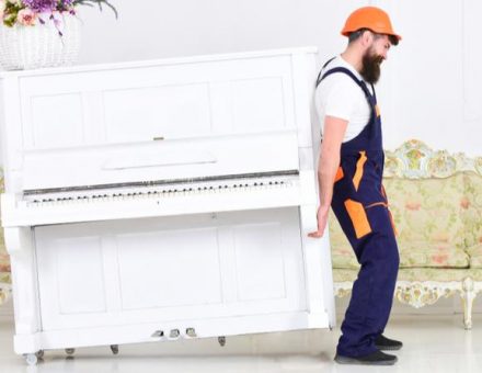 Mover in hard hat struggling to move a fragile piano by himself