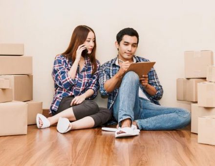 Couple sitting in a room full of boxes doing their moving prep: making a checklist and calling their moving company