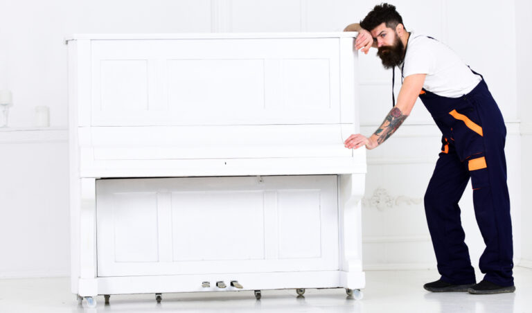 A man wipes his brow while struggling to move a piano.