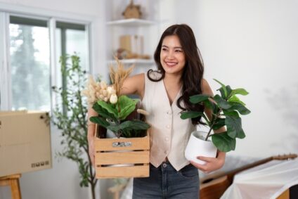 A young woman smiles while holding houseplants.