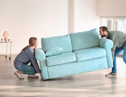 Couple struggling to carry a couch across the floor of their new home