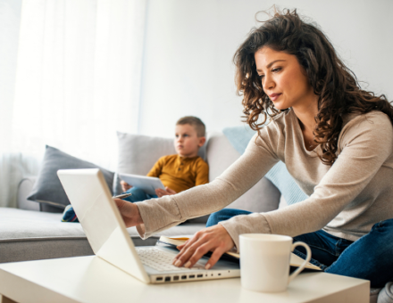 Young woman working from home during the COVID-19 pandemic with her child next to her on the couch.