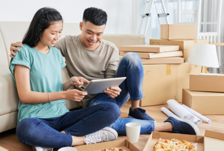 Man and woman sitting on the floor leaning on sofa with pizza and drinks after moving day