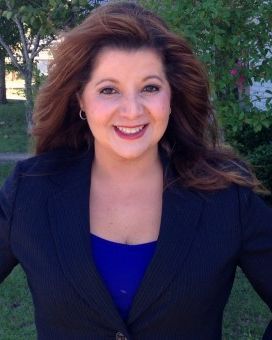 woman in a black blazer and blue top smiling