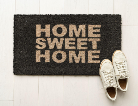 Door mat reading “home sweet home” with white tennis shoes in the corner