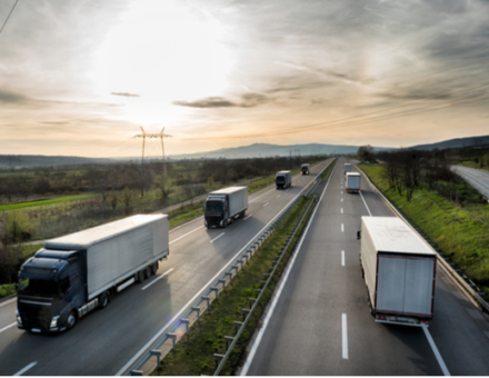 A group of trailer trucks drive down the interstate during sunset.