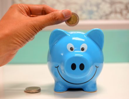 A closeup of a hand putting a coin into a piggy bank.