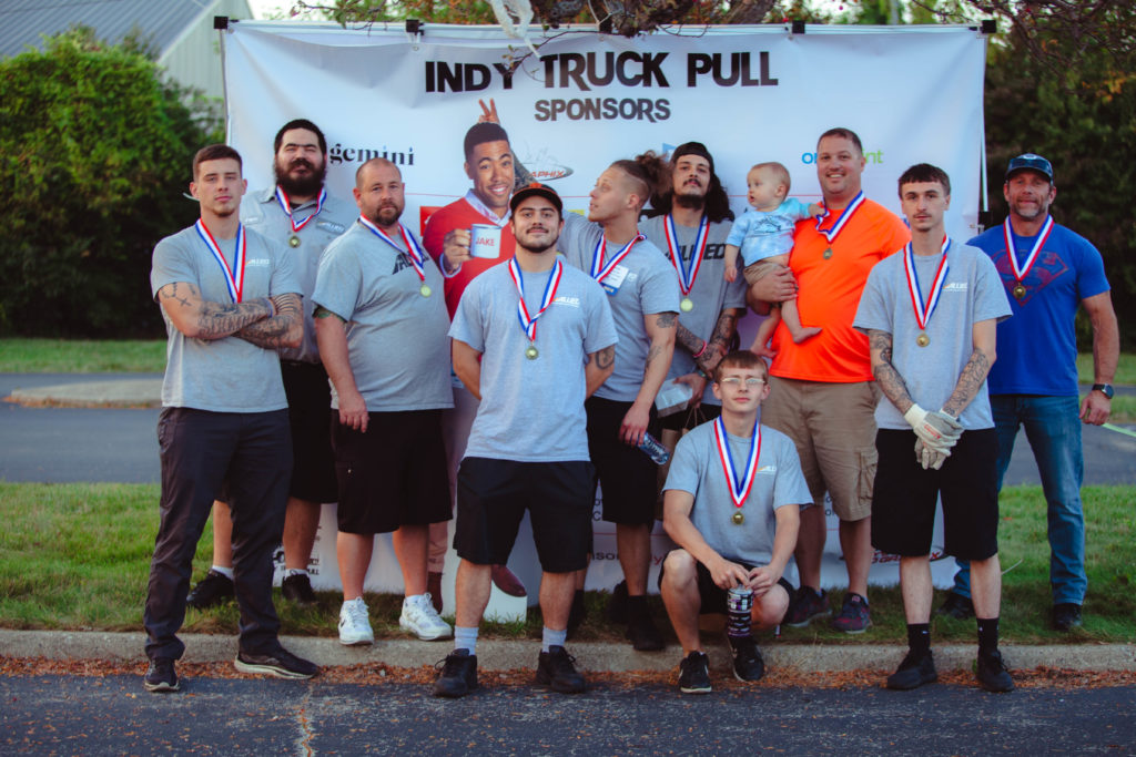 Winning team of the Indy Truck Pull pose in front of the sponsor sign