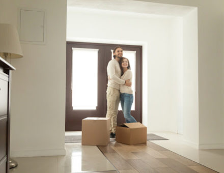 Happy young millennial couple hugging standing near boxes moving into new home.