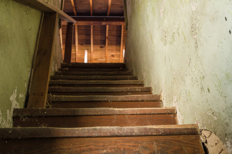 Creepy staircase with spiderwebs and crumbling walls.