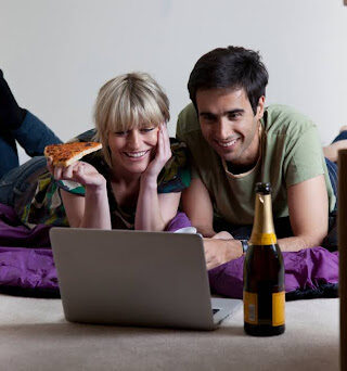 Young couple eats pizza on floor and watches movie on computer after moving in.