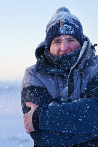 A person wearing winter clothes shivering as it snows.