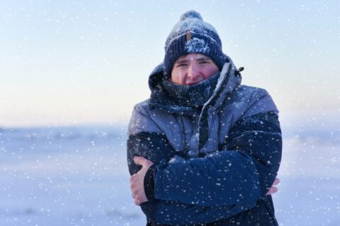 A person wearing winter clothes shivering as it snows.