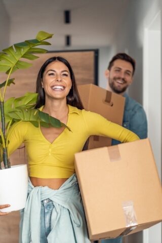 Two people carrying boxes and smiling.