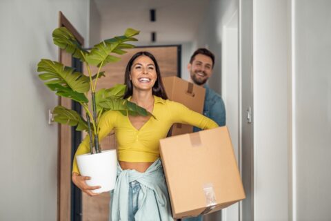 Two people carrying boxes and smiling.