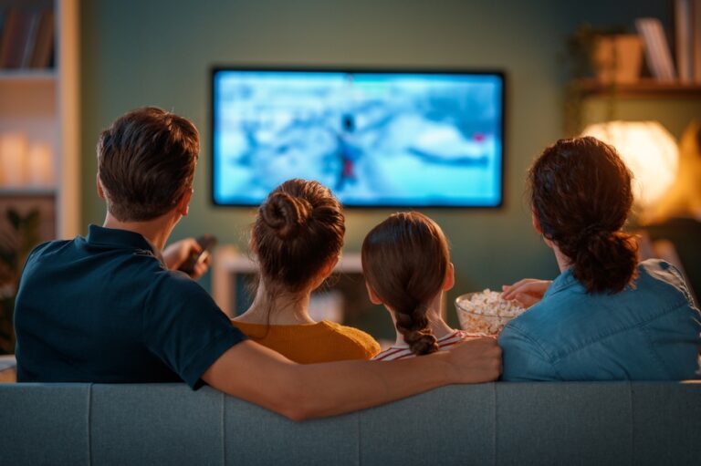 The back of a family's heads as they watch a movie on a couch.