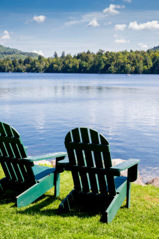 Two empty green chairs in front of a shimmering lake.