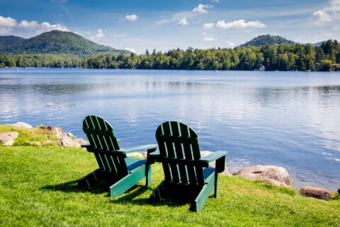 Two empty green chairs in front of a shimmering lake.