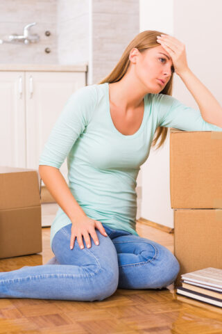Person sitting on the ground with their head in their hands, surrounded by boxes.