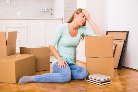 Person sitting on the ground with their head in their hands, surrounded by boxes.