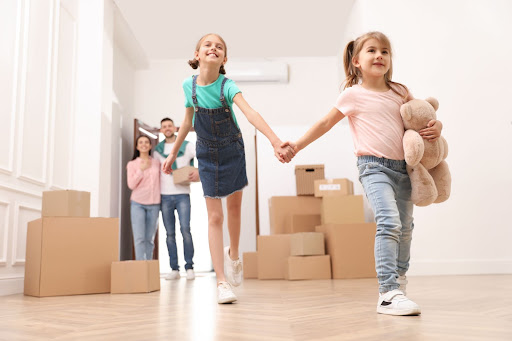Children holding hands and smiling after moving into their new house.