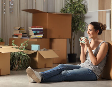 Happy tenant resting drinking coffee moving home sitting on the floor in the night.