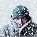 A person wearing winder clothes shivering as it snows.