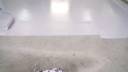 A paint roller painting a floor white.