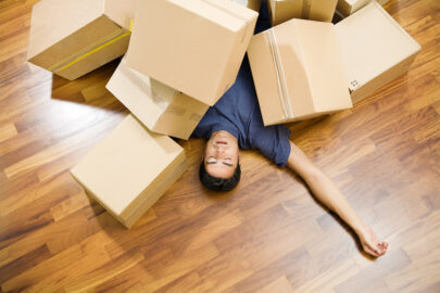 tired man laying on hardwood floors covered in moving boxes