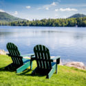 Two empty green chairs in front of a shimmering lake.