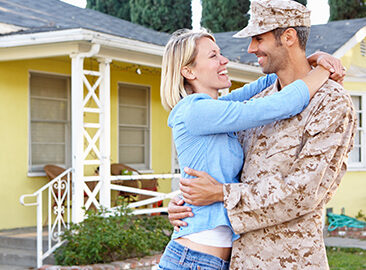 military couple hugging in front of their home