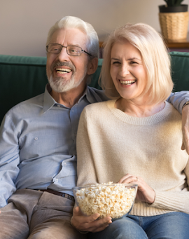 A smiling senior couple eating popcorn and watching tv on their couch.