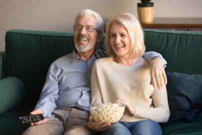A smiling senior couple eating popcorn and watching tv on their couch.