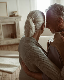 tender senior husband and wife embracing and looking at their home, moving out concept