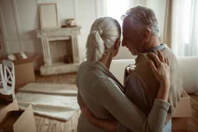 tender senior husband and wife embracing and looking at their home, moving out concept