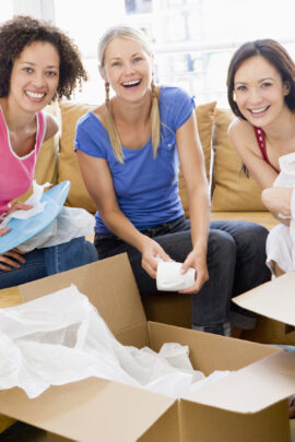 Three girl friends unpacking box's in new home smiling to camera