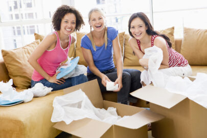 Three girl friends unpacking box's in new home smiling to camera