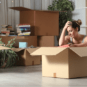 Person sitting on the ground with their head in their hands, surrounded by boxes.