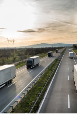 A group of trailer trucks drive down the interstate during sunset.