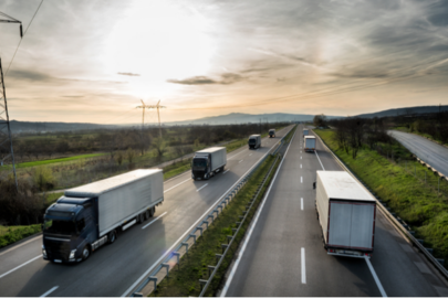 A group of trailer trucks drive down the interstate during sunset.