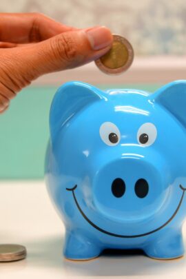 A closeup of a hand putting a coin into a piggy bank.