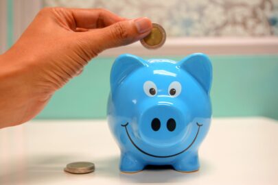 A closeup of a hand putting a coin into a piggy bank.