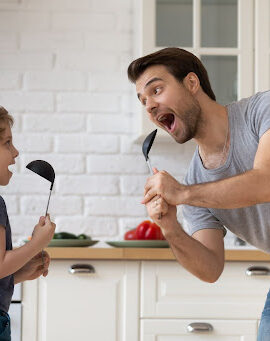 Parent and child sing in the kitchen using spoons as microphones.